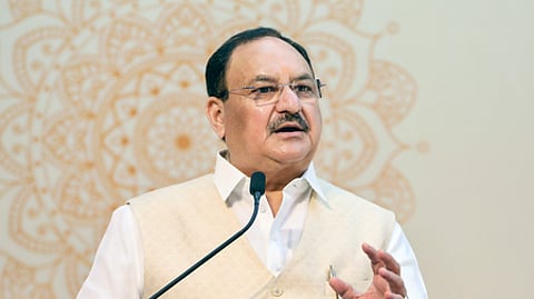 Image featuring JP Nadda, wearing a cream vest and white shirt, speaking at a podium with a microphone, gesturing with his hand during a speech