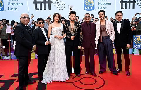A group of six people, dressed in formal attire, stand on a red carpet at the Toronto International Film Festival (TIFF).