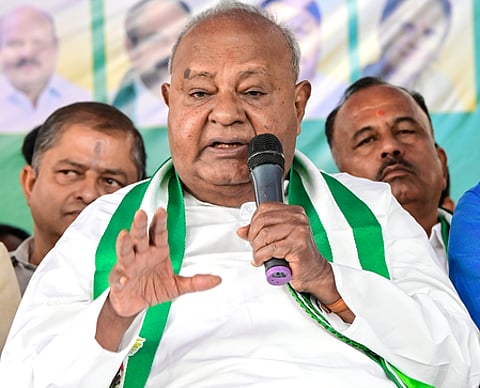 Former prime minister HD Deve Gowda seated on a chair at a stage, speaking with a mic held in his left hand