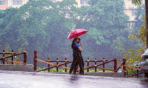Two school girls hold a single umbrella and walk in the rain