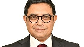 A professional headshot of a middle-aged man with short, dark hair and round, black-framed glasses. He is smiling warmly at the camera, wearing a dark suit jacket, a crisp white dress shirt, and a maroon tie featuring small, repeating crest emblems.