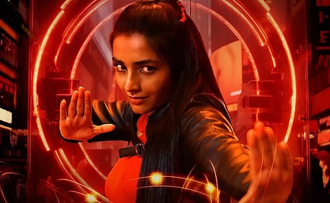 Actor Rajisha Vijayan stands with her hands raised in a stylised pose, framed by glowing red circular lights in a futuristic setting.