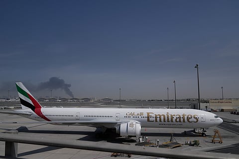A plume of smoke caused by an Iranian strike is seen in the background an an Emirates plane is parked at the Dubai International Airport after its closure in Dubai, United Arab Emirates, Sunday, March 1, 2026.