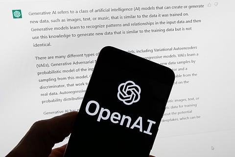The OpenAI logo is displayed on a mobile phone in front of a computer screen with output from ChatGPT, March 21, 2023, in Boston.