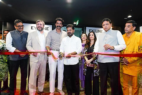 An image showing a group of prominent figures at a ribbon-cutting ceremony for the inauguration of Eyeline Studios (a Netflix company) in Hyderabad.
Centrally located, Revanth Reddy (Chief Minister of Telangana) is seen cutting a bright red ribbon with a pair of scissors. He is flanked by actor Rana Daggubati to his right and other dignitaries and executives on both sides. The background features the "EYELINE" logo on the walls. The atmosphere is professional and celebratory, with several attendees smiling as the ribbon is cut.