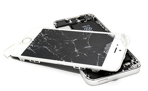 An iPhone with a severely shattered screen, detached from its silver casing. The internal components, including the battery, are visible in the background.