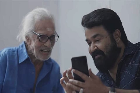 Painter Namboodiri on the left and actor Mohanlal on the right looking at the phone together.