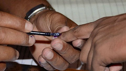 A close up picture of three hands, one putting ink on the another. Indicating the polling process.