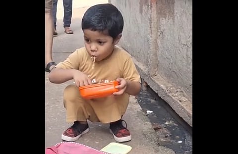 little boy eating his tiffin on road side