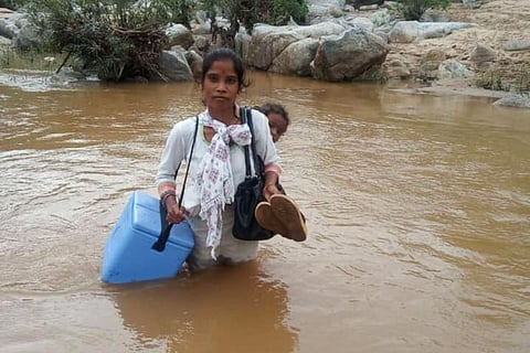 Lugging a vaccination box and carrying a child on her back, an ASHA worker on her way to vaccinate people, wades through a water stream