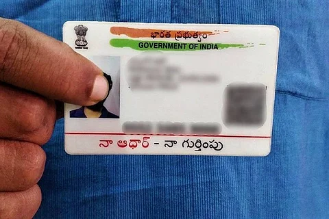 A person holding up an Aadhaar card, information blurred out