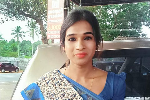 Democratic Social Justice Party candidate from Vengara Anannyah Kumari Alex in a blue and white sari, her hair tied behind her. Behind her is a car and some trees further behind.
