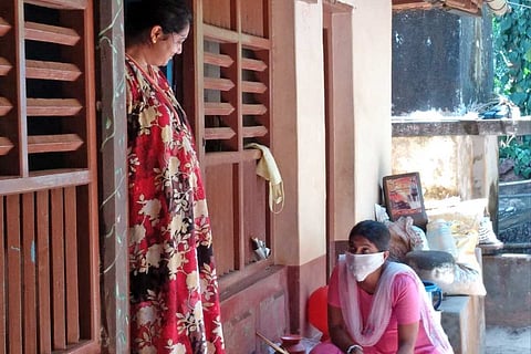 An ASHA worker sitting outside a house and taking down the details from a woman