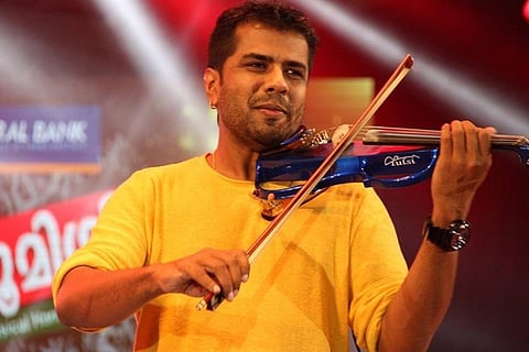 Late violinist Balabhaskar. He wears a yellow t-shirt and is playing a violin on stage during a program