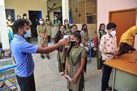 Staff member checking temperature of a girl student in a school
