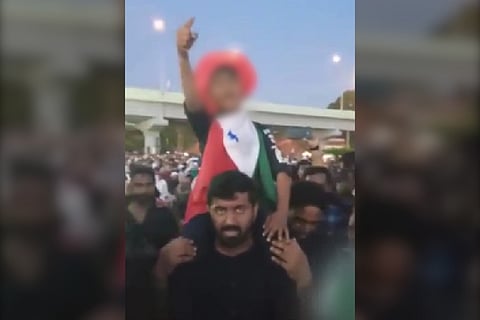 A sloganeering boy draped with PFI flag seen sitting on a man's shoulders and raising his hand