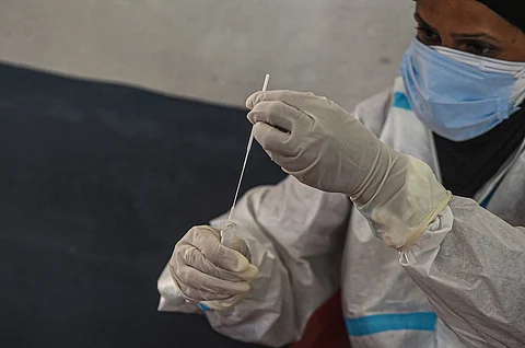 A health worker wearing PPE holding a COVID-19 test swab
