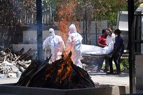 A funeral pyre burns as two men in PPE kits unload a body from the back of a vehicle with the help of two other men
