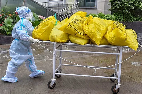 A person in PPE kit wheeling a trolley full of yellow bags