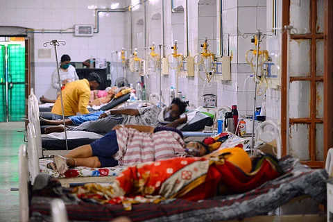Patients lying on beds in a hospital ward with drips hanging on the right and some attenders behind