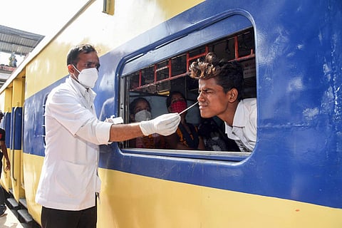 A health worker takes swab sample of a passenger sitting inside a train for COVID-19 test.