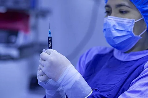 A woman health professional wearing PPE and holding injection.