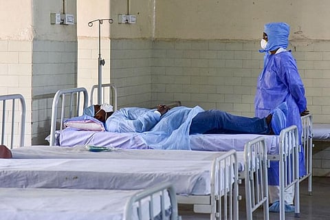 Man lying down in a covid isolation ward with a health worker standing at the end of the bed