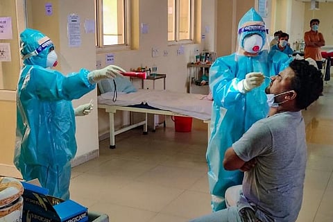 A health worker in a PPE suit checking nasal swab sample from a man for coronavirus test