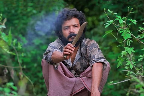 A shot from the film where actor Sreenath Bhasi is squatting staring at a knife