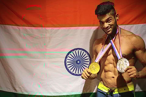 Chennai bodybuilder Manikandan posing with his medals behind Indian flag.