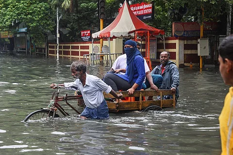 A man pushes his rickshaw with passengers through a flooded street in Chennai in front of a police station