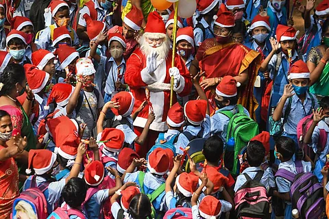 A man dressed as Santa Claus surrounded by school children wearing red hats