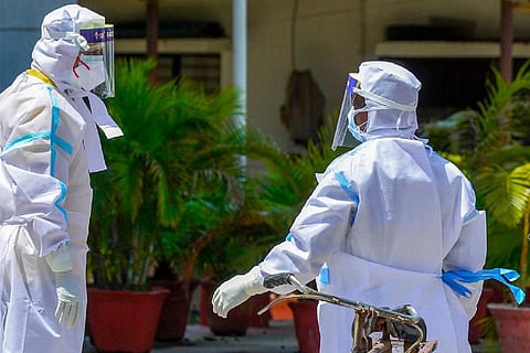Healthcare Workers, keeping physical distance, talking to each other in Personal Protection Kit outside a hospital