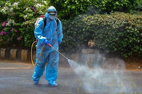 A person in a PPE kit spraying disinfectant on the street