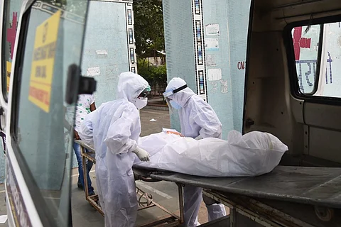 Two people in full white ppe suits putting a body wrapped in white in an ambulance.