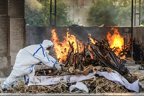 A crematorium worker wearing full PPE adjusts a log in a funeral pyre that has been lit