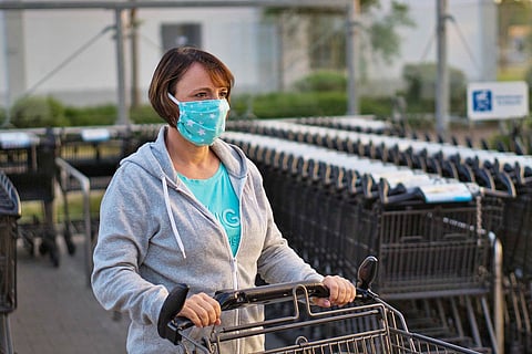 A woman wearing a mask pushes a shopping cart