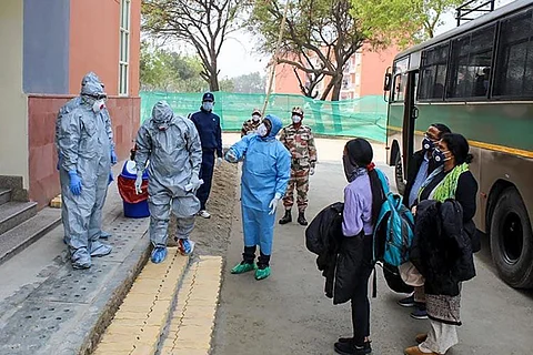 Medical professionals in PPE kits standing before a hotel