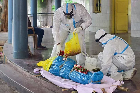 People wearing PPE kit keeping flowers on a dead body of a COVID-19 victim before cremation