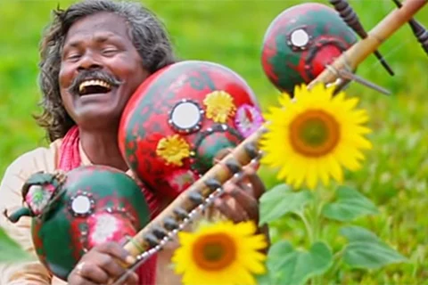 Kinnera artist Darshanam Mogulaiah with his instrument in a sunflower field