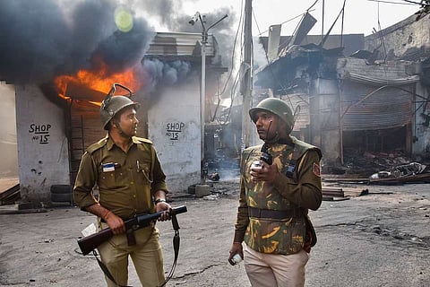 Police stand in front of a burning shop during the Delhi riots