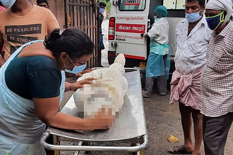A mother crying over the dead body of her son while the body is being taken into ambulance