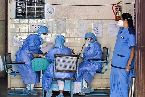 Four healthcare workers sitting at a desk in a hospital while wearing PPE suits