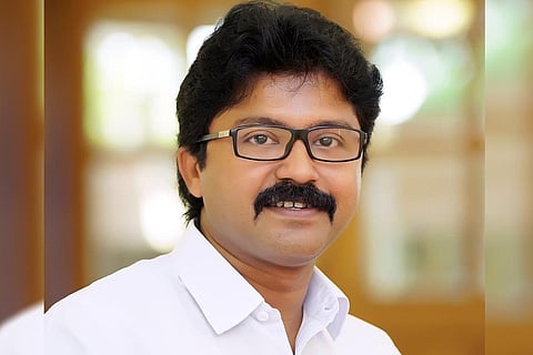 Eldhose Kunnappilly MLA. He is wearing a white shirt, looks straight ahead to the camera with a sight smile