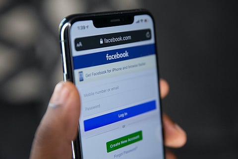 Man holding up a mobile phone with Facebook login page on screen