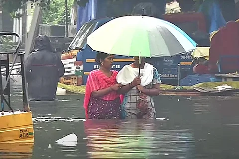 Two women walking through waist-deep water holding up an umbrella