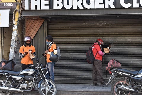 Deliverymen of food aggregators Swiggy and Zomato wait outside a food outlet to collect their orders during nationwide Covid lockdown