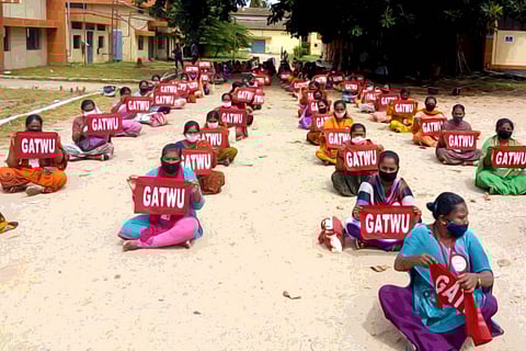 GATWU protest: Women sitting in four lines at fixed distance wearing black masks and holding up a cloth reading 'GATWU'