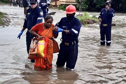 A woman being helped across flood waters by rescue personnel