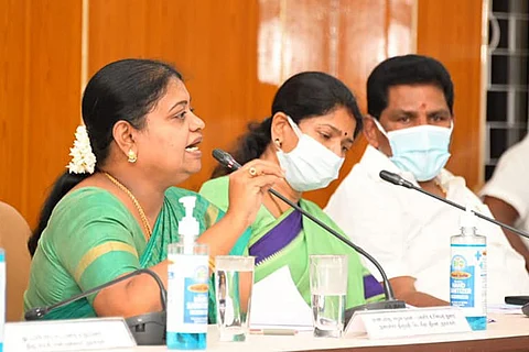 DMK Minister Geetha Jeevan speaks into a mic, as Kanimozhi and another man sit beside her 